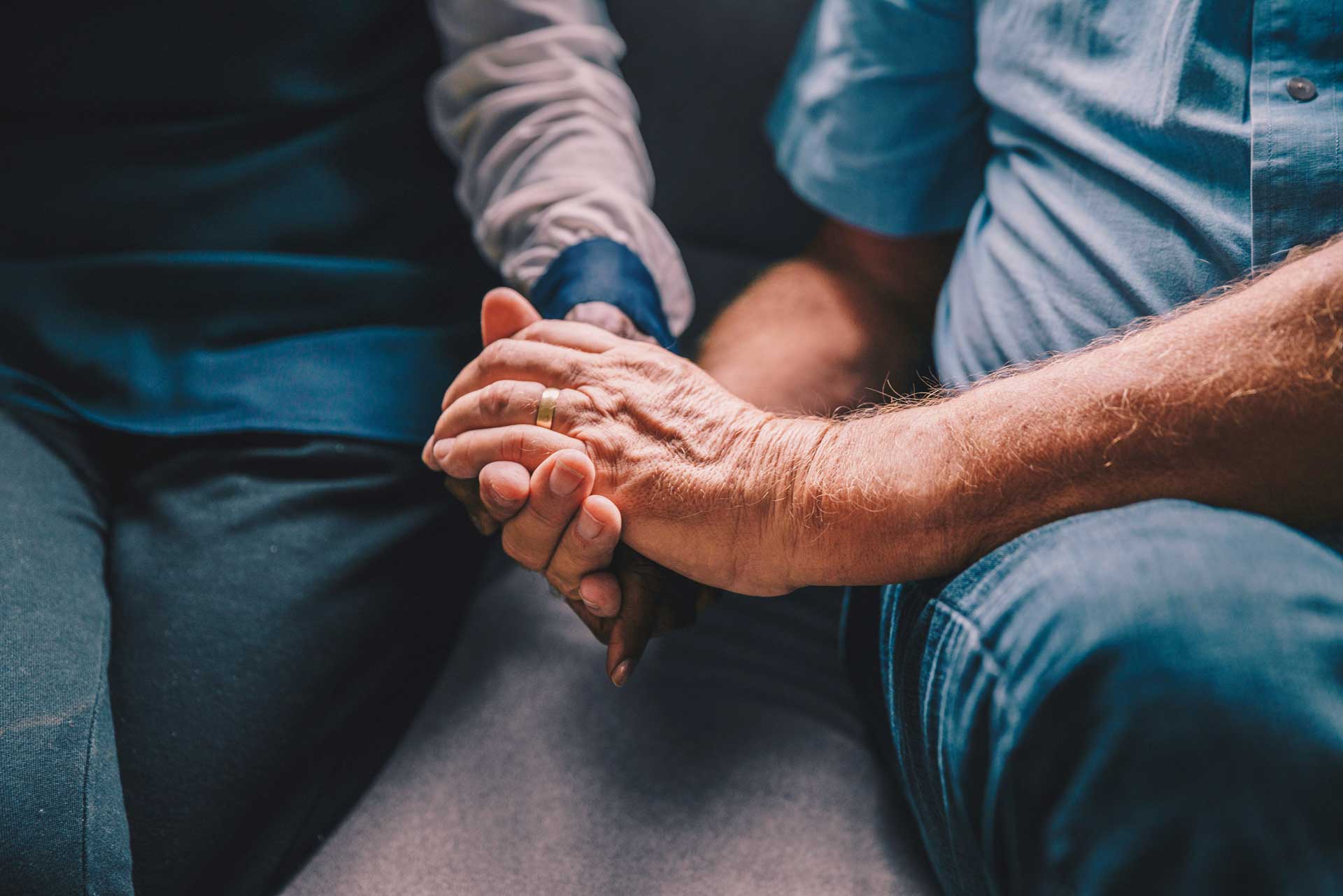 older man and woman holding hands while sitting