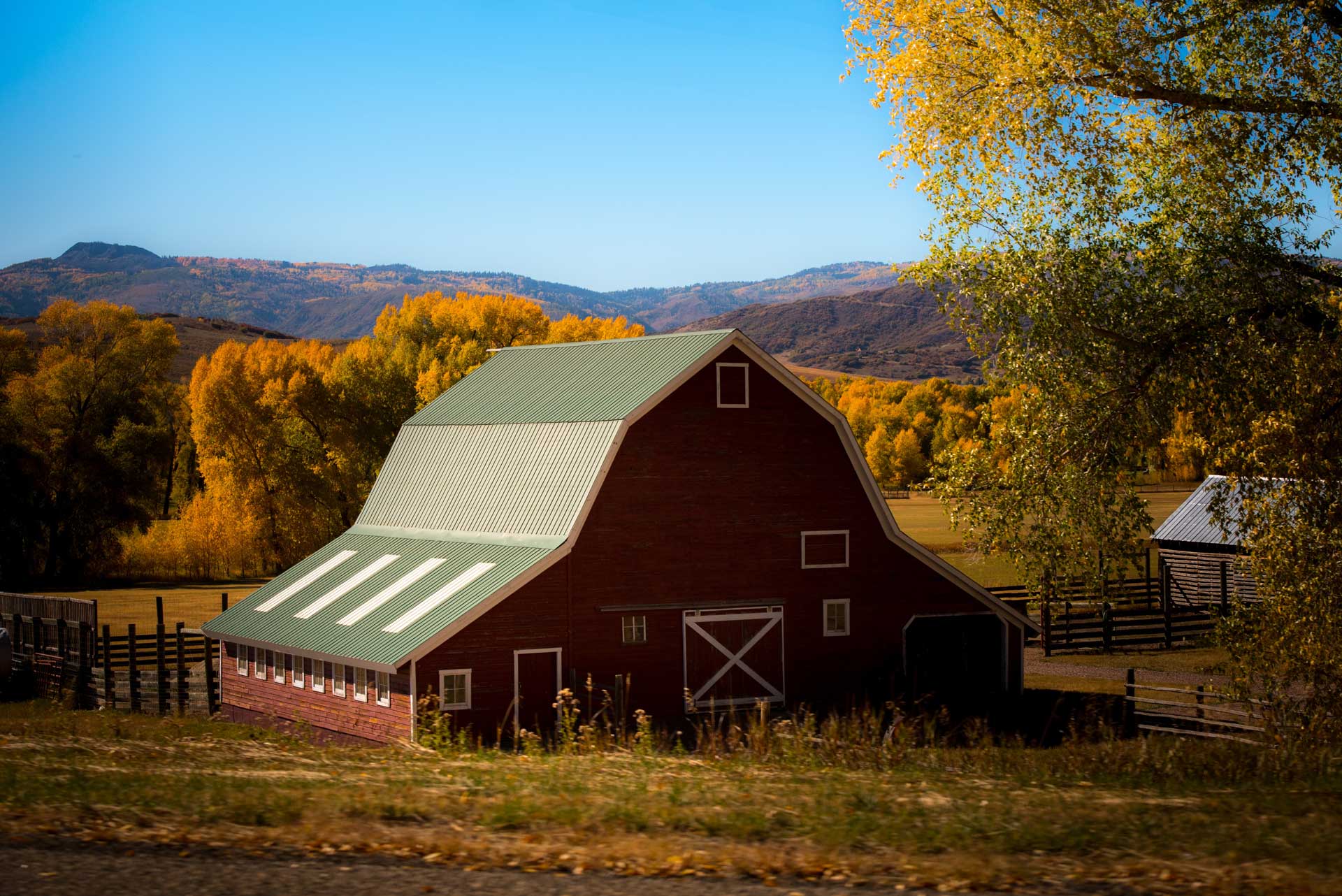 red barn with green roof surrounded with trees in the distance during fall